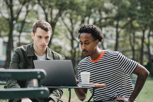 Concentrated young multiethnic male colleagues in casual clothes sitting in outdoor cafe and working remotely on laptop during coffee break