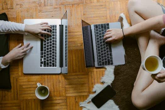 From above of crop unrecognisable female friends typing while studying on laptops remotely and enjoying tea on floor in cozy living room