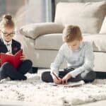 Full body of focused children coworkers working on project taking notes in organizers at home