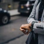 Crop unrecognizable punctual black businessman in formal outfit checking time on sidewalk in modern city