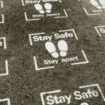 From above white sign of feet and inscription Stay Safe Stay Apart painted on asphalt road during coronavirus outbreak