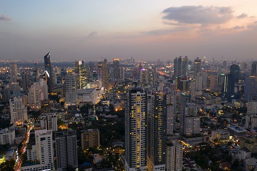Remote picturesque scenery of contemporary city center with glowing skyscrapers and modern towers and buildings against cloudy sundown sky