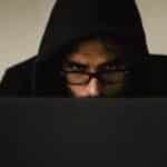 Serious young male programmer wearing black hoodie browsing netbook and hacking software in studio