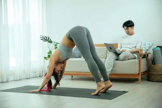 Flexible ethnic woman practicing Adho Mukha Svanasana yoga pose at home near boyfriend
