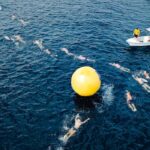 Aerial view of swimmers taking park in race and swimming around big yellow inflated ball in sea water