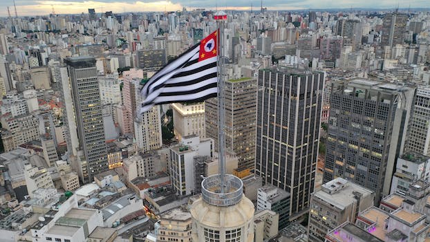 Aerial view of Sao Paolo flag waving on wind on skyscraper spire in urban metropolis district in daylight