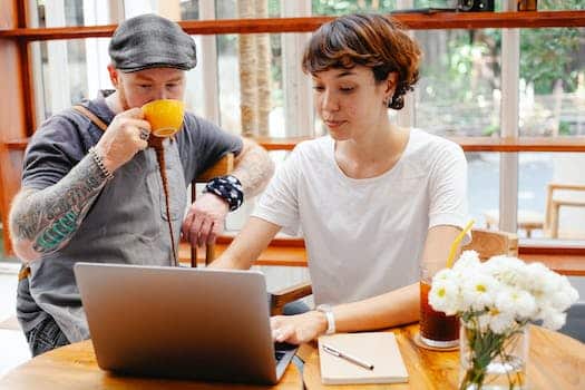 Pensive young woman typing on netbook while man with cup drinking coffee at table of cafe