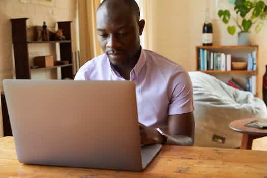 Concentrated African American male typing information on netbook at wooden table in cozy living room