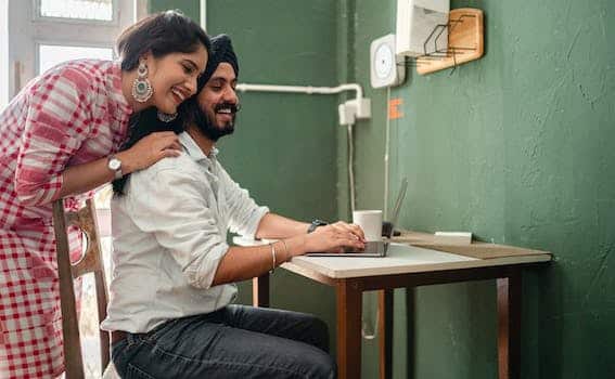 Happy young cuddling Indian couple using laptop during work at home