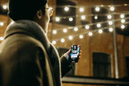 Selective Focus Photography of Man Using Smartphone Beside String Lights